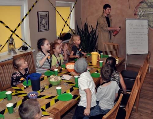 Zdjęcie przedstawia dzieci podczas przyjęcia urodzinowego w pokoju Małego Detektywa. Animator otwiera szampana.