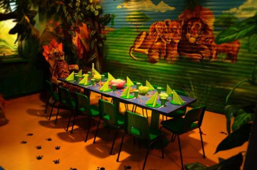 Na zdjęciu widać zastawiony stół w pokoju urodzinowym Dżungla. Stół przygotowany jest na przyjęcie urodzinowe.